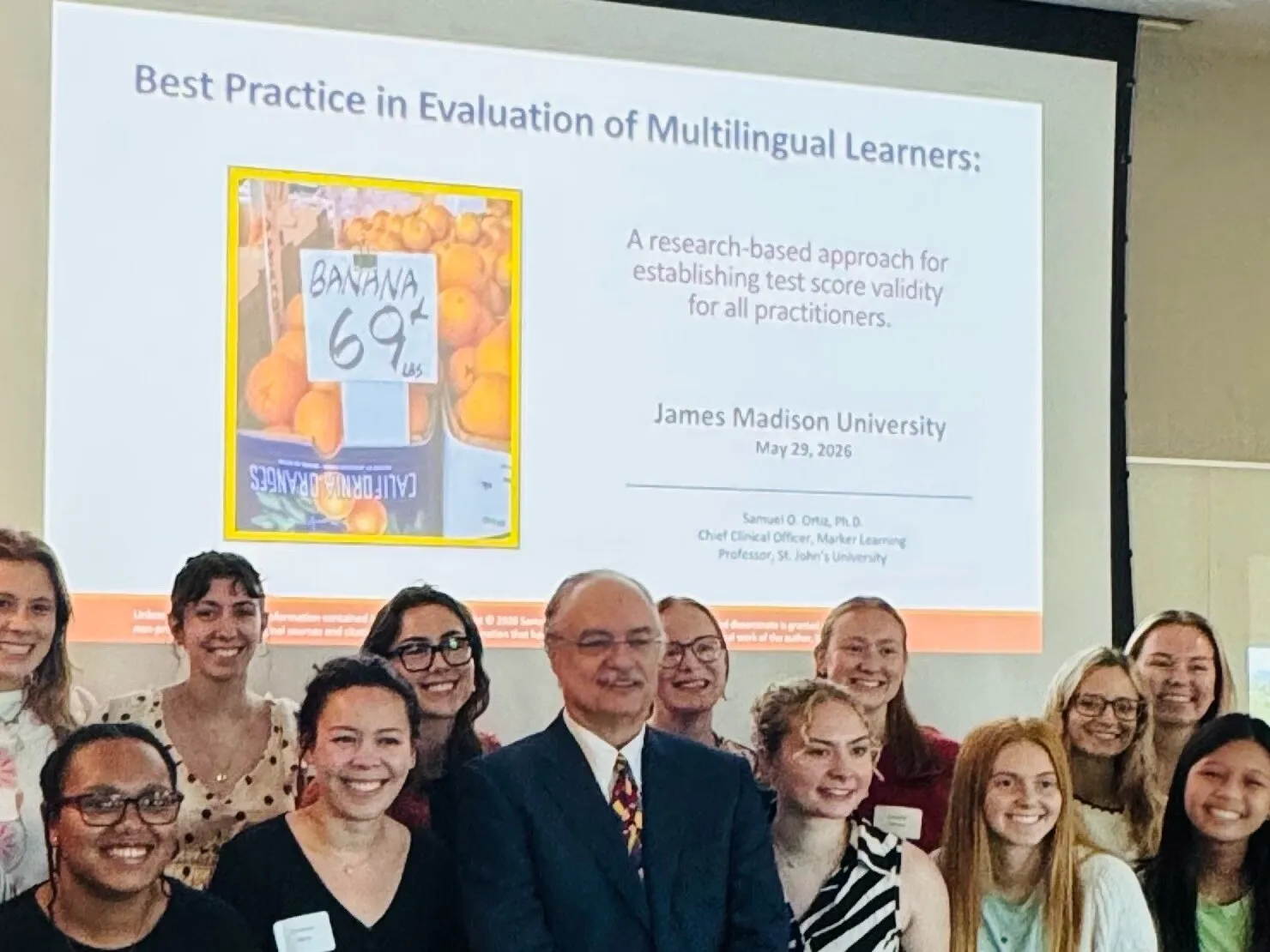 Dr. Ortiz standing with a group of students in front of a projected slide titled Best Practice in Evaluation of Multilingual Learners.